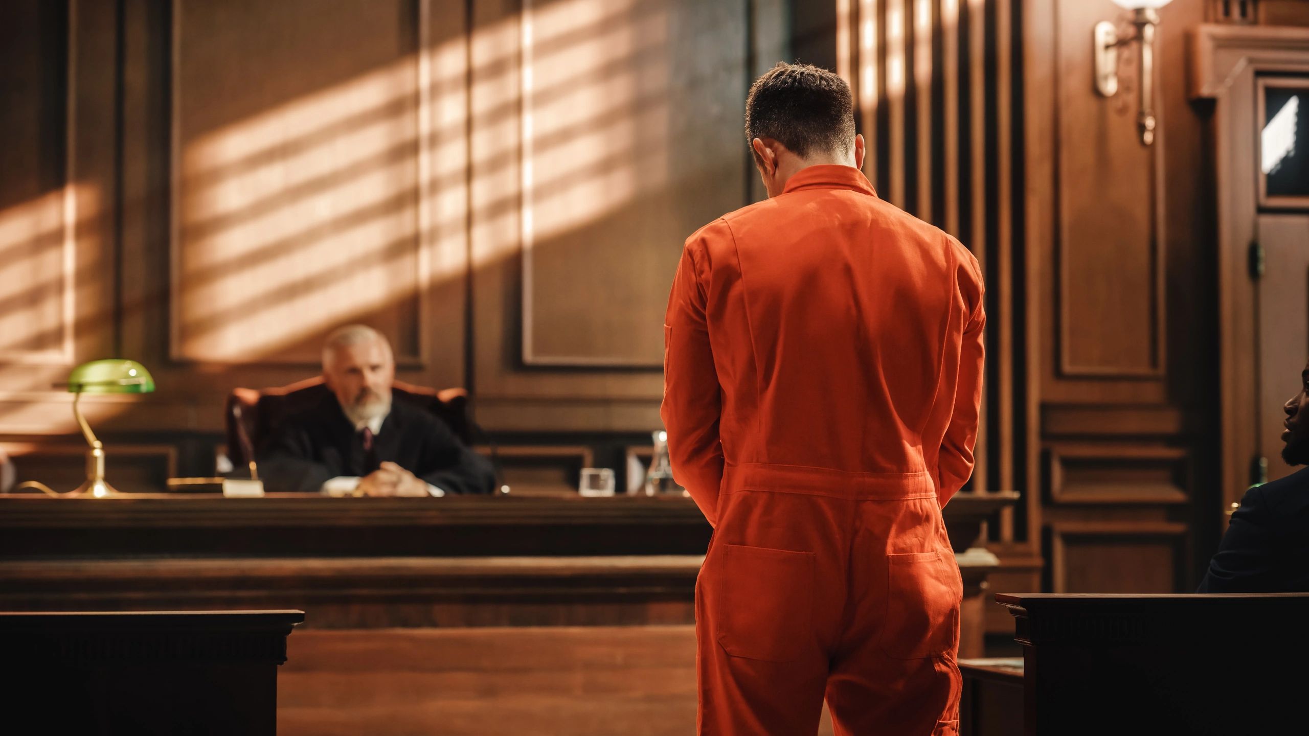 Defendant in orange suit facing judge in courtroom.