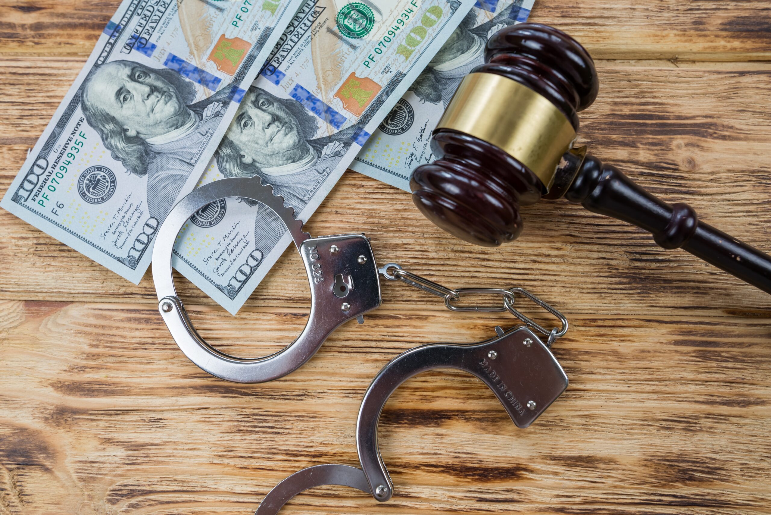 Handcuffs, money, and a judge's gavel on a wooden surface.